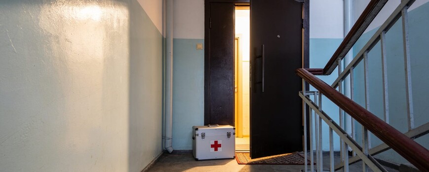 Медицинский чемоданчик у приоткрытой двери квартиры на лестничной площадке
